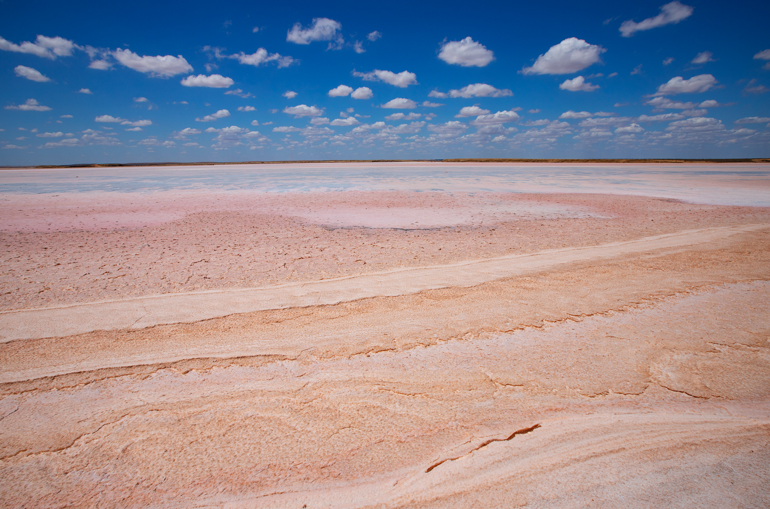 An image of a scenic beach with light pinkish beige sand and a fluffy clouds in the background.