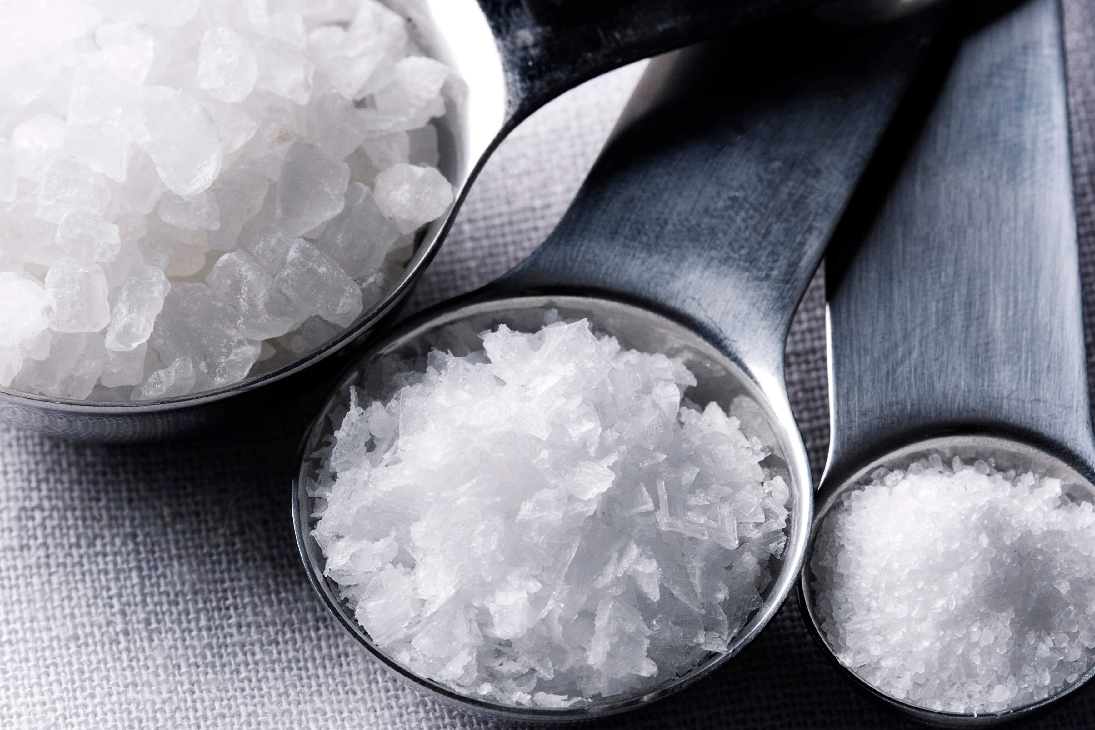 An image of coarse, medium and fine salt grains in three different measuring spoons of decreasing size.